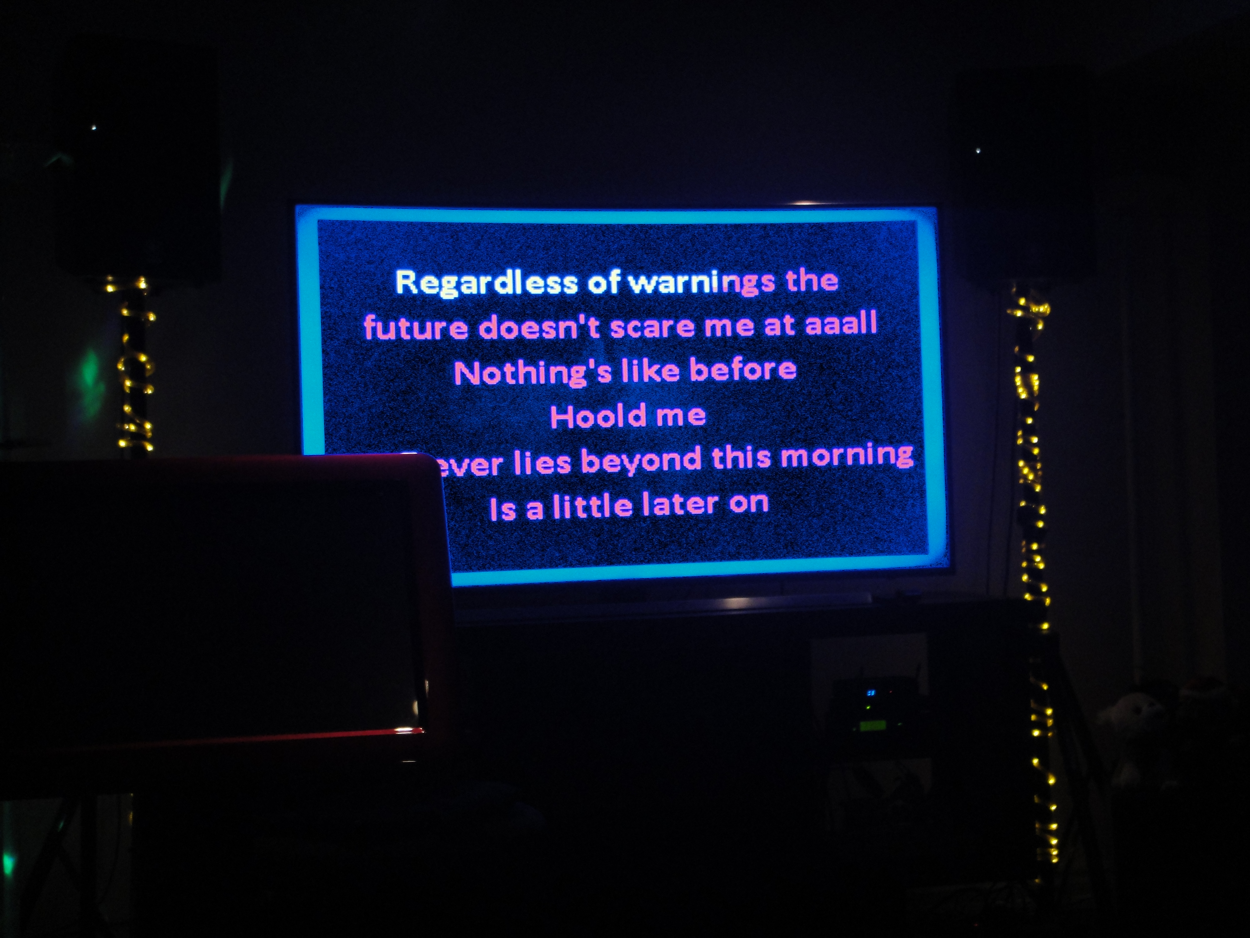 Dark scene with a lit up karaoke screen with the text
                'Regardless of warnings the future doesn't scare me at aaall Nothing's like before Hoold me
                whatever lies beyond this morning is a little later on' from Utada Hikaru's Simple and Clean